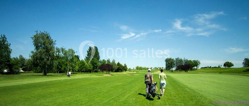 Deux personnes marchant sur un terrain de golf verdoyant sous un ciel bleu clair.