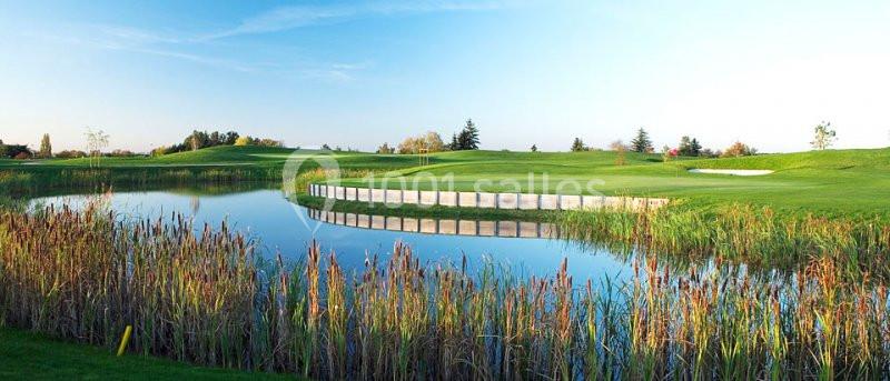 Étang entouré de roseaux avec un terrain de golf verdoyant en arrière-plan sous un ciel dégagé.
