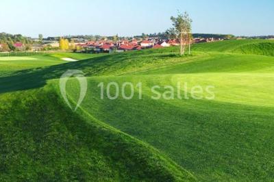 Paysage de terrain de golf avec pelouses verdoyantes, drapeau sur le green et maisons en arrière-plan.