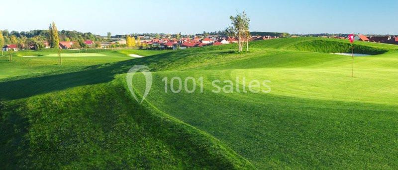Paysage de terrain de golf avec pelouses verdoyantes, drapeau sur le green et maisons en arrière-plan.