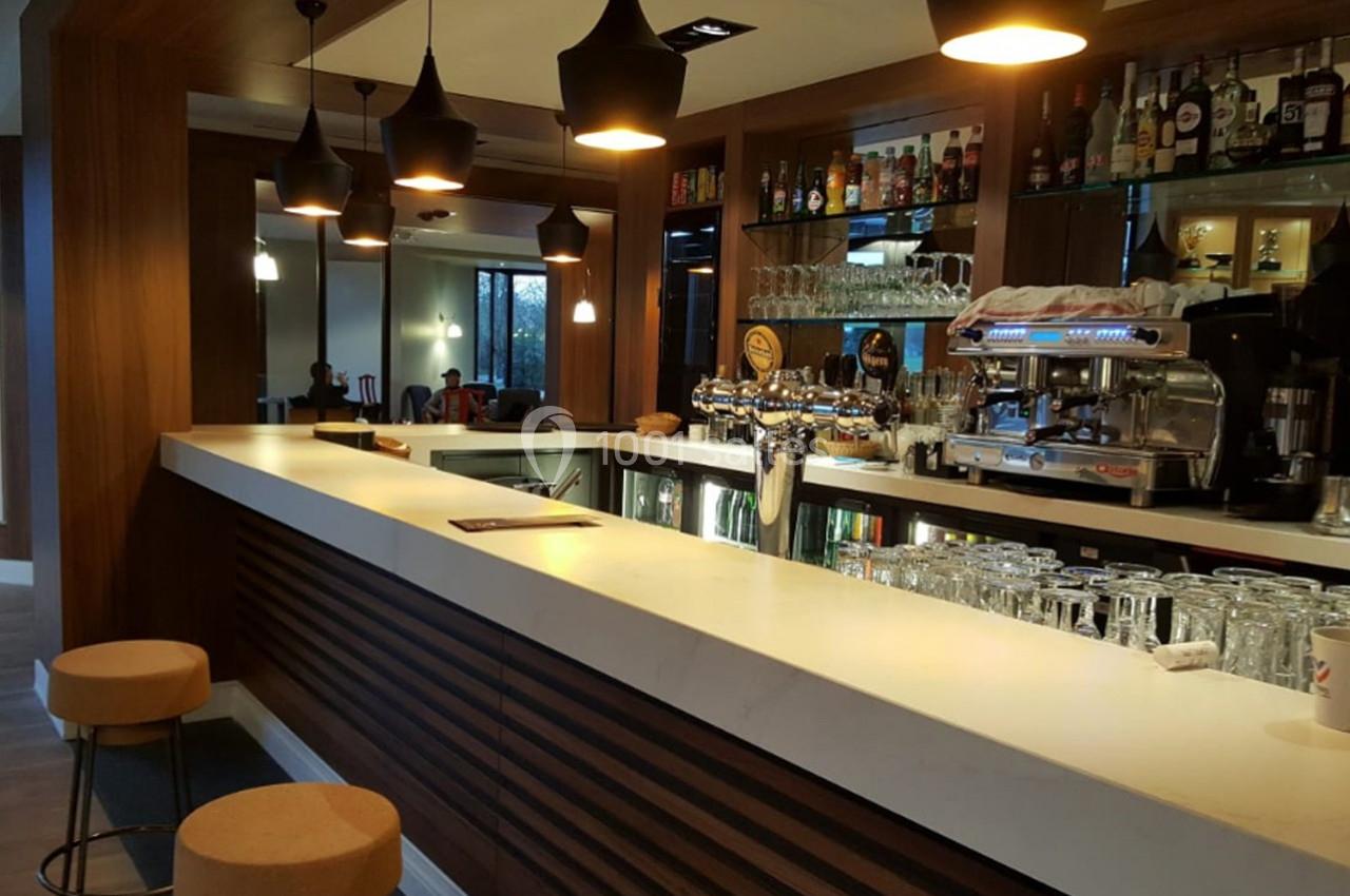 Bar moderne avec comptoir en marbre blanc, tabourets en bois, luminaires suspendus et étagères garnies de bouteilles.