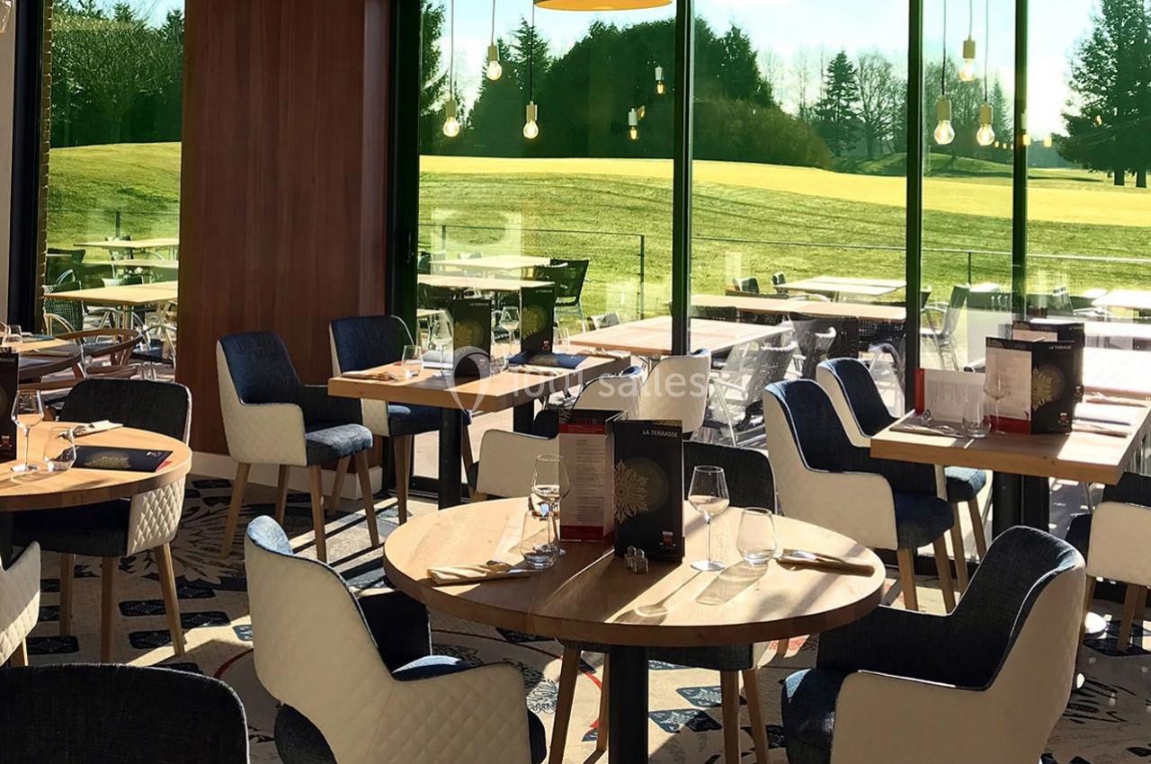 Salle de restaurant lumineuse avec des tables dressées, donnant sur un espace extérieur verdoyant.