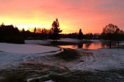 Paysage hivernal avec un terrain enneigé, des tables extérieures et un coucher de soleil vibrant au-dessus d'un lac.