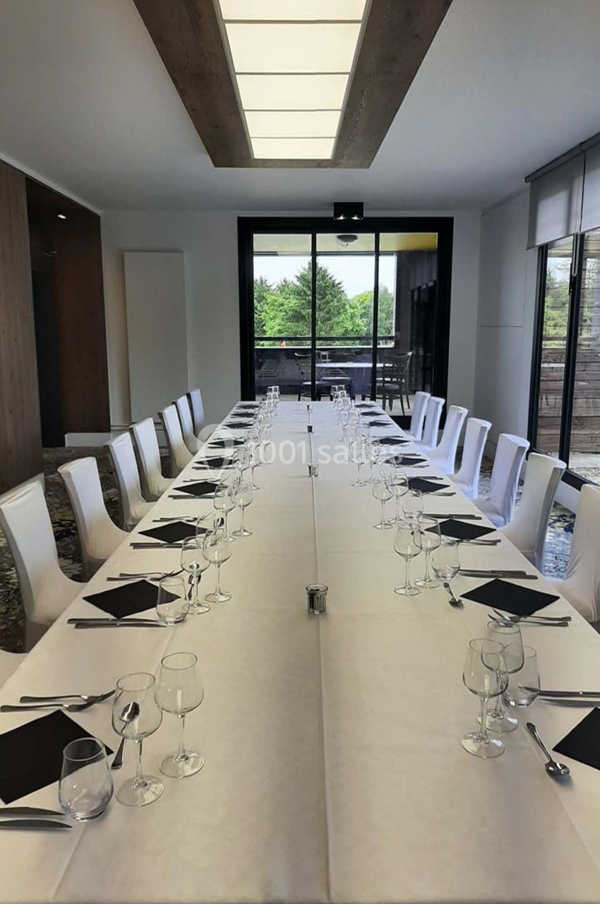 Salle de réunion avec une longue table dressée, couverts et verres alignés, éclairée par une grande baie vitrée.