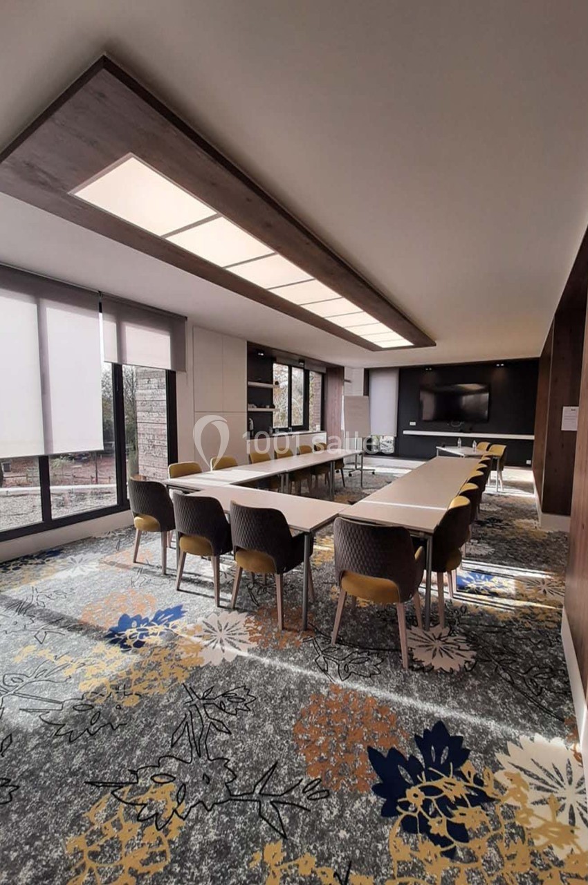 Salle de réunion lumineuse avec une grande table rectangulaire, chaises modernes et écran mural.