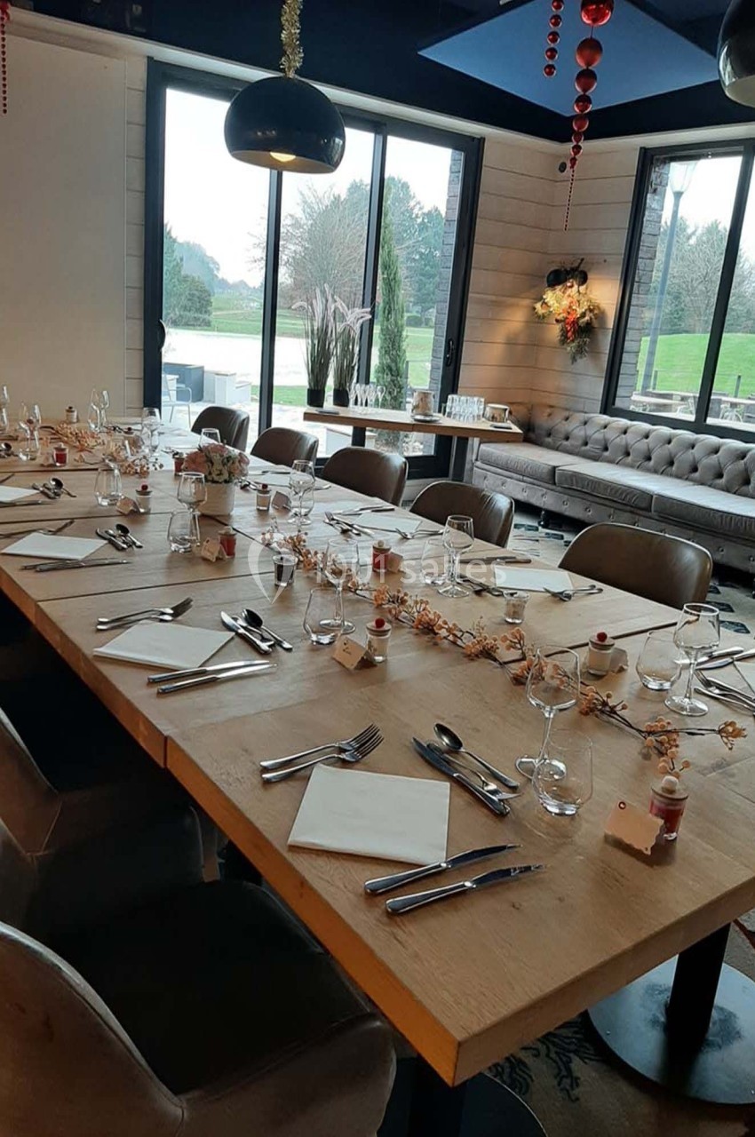 Table en bois dressée pour un repas, avec couverts, verres et décorations, dans une salle lumineuse avec vue sur un jardin.