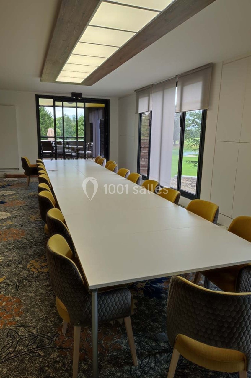 Salle de réunion lumineuse avec une grande table blanche entourée de chaises jaunes et grises, vue sur un espace extérieur…