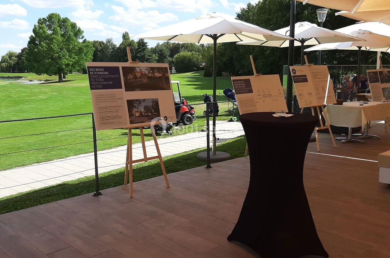 Des panneaux d'exposition sur des chevalets sont disposés sur une terrasse surplombant un terrain de golf verdoyant.