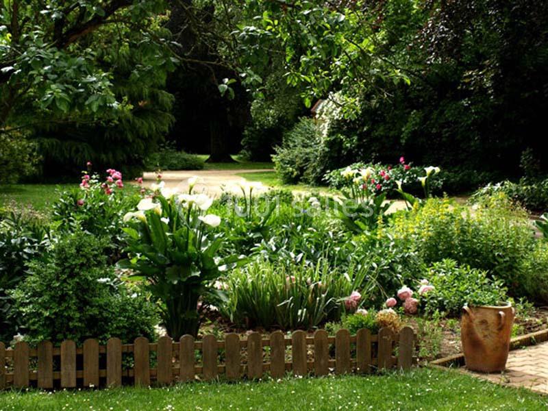 Jardin verdoyant avec fleurs colorées, petite clôture en bois et pot en terre cuite au premier plan.