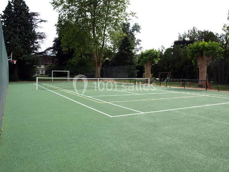 Terrain de sport extérieur avec marquages pour le tennis et le basketball, entouré d'arbres et d'une clôture.
