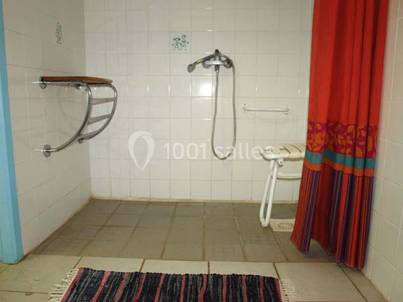 Douche accessible avec barre d'appui, siège pliant, rideau coloré et tapis au sol.