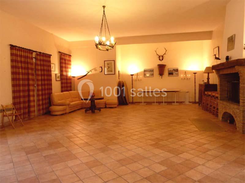 Grande pièce avec sol en carrelage, cheminée en pierre, canapé, rideaux à carreaux et décoration murale rustique.