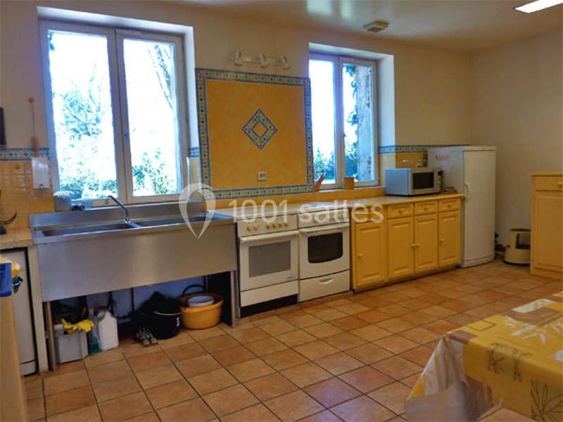 Cuisine spacieuse avec meubles jaunes, évier double, cuisinière, réfrigérateur, micro-ondes et carrelage au sol.