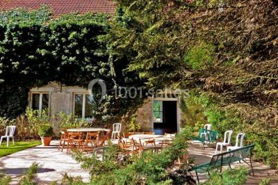 Terrasse ensoleillée avec tables et chaises en bois, entourée de verdure et d'une façade recouverte de lierre.
