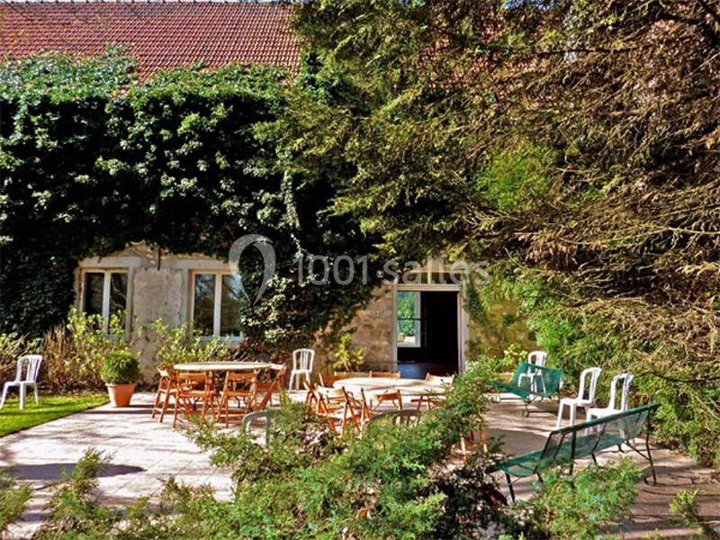 Terrasse ensoleillée avec tables et chaises en bois, entourée de verdure et d'une façade recouverte de lierre.