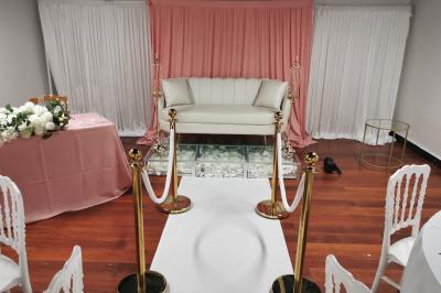 Canapé blanc devant un rideau rose, entouré de bougeoirs dorés en forme de cages et d'une table en verre.