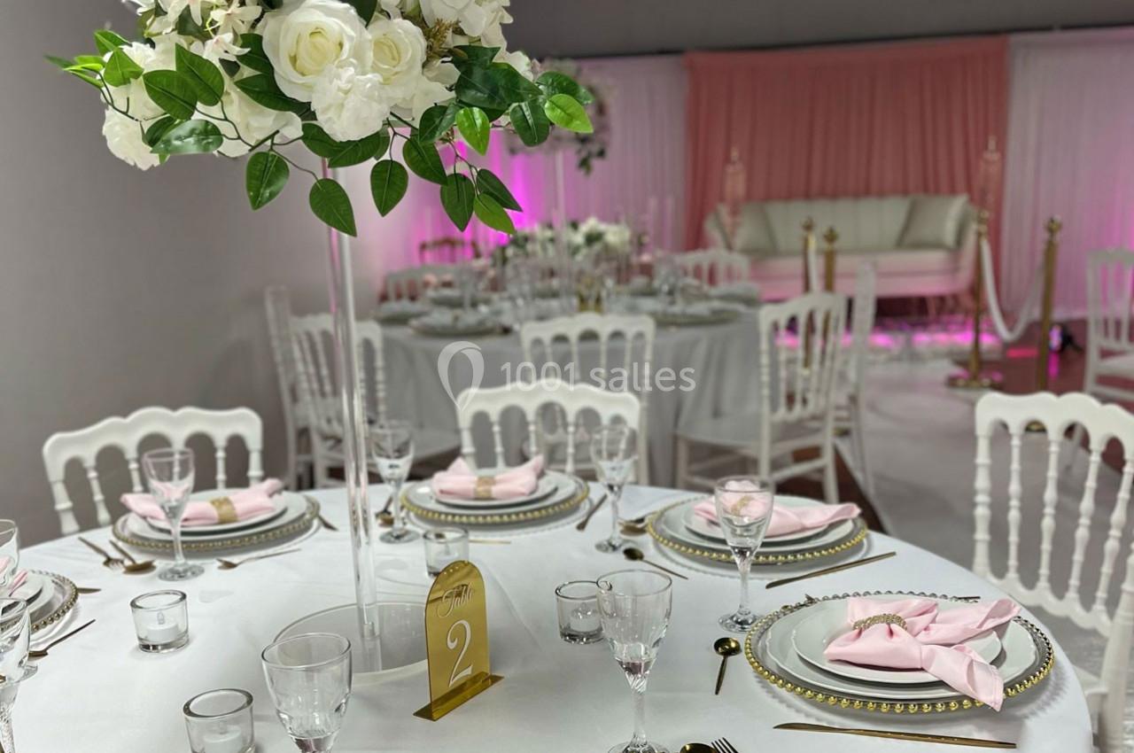 Salle de réception décorée avec des tables élégantes, nappes blanches, serviettes roses et centre de table floral.