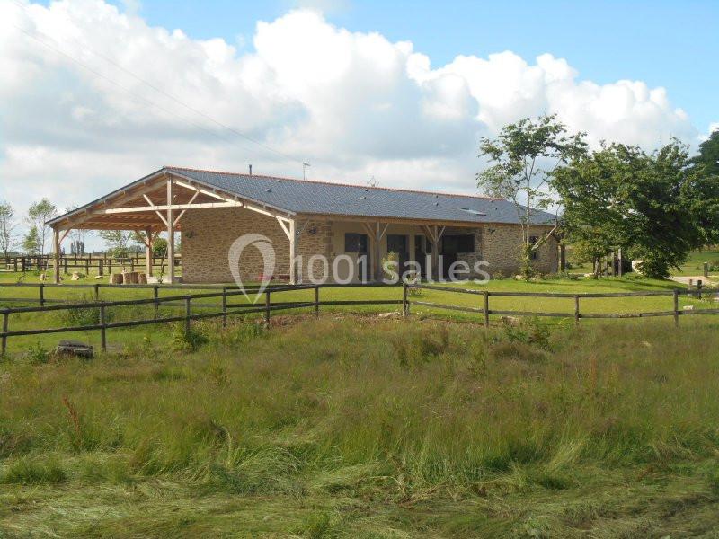 Bâtiment en pierre avec toit en tuiles, entouré de pelouse, clôtures en bois et quelques arbres sous un ciel partiellement…