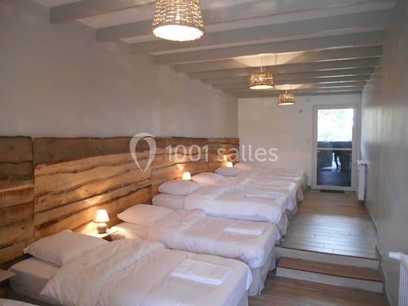 Dortoir lumineux avec plusieurs lits simples alignés, murs en bois et éclairage suspendu.