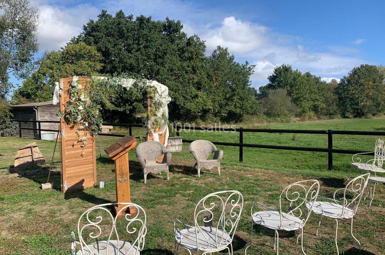 Chaises blanches disposées en extérieur devant une arche décorée de fleurs et feuillages, dans un cadre champêtre.