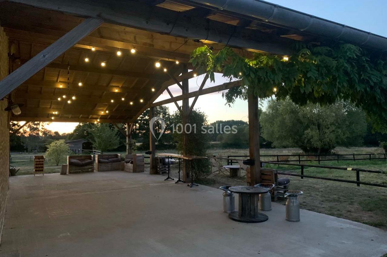 Structure en bois éclairée par des guirlandes lumineuses, avec vue sur un paysage champêtre au crépuscule.