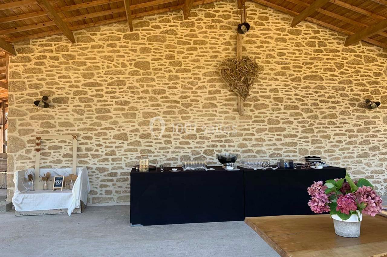 Mur en pierre apparente avec une table de buffet noir, des plats disposés et un bouquet de fleurs roses au premier plan.