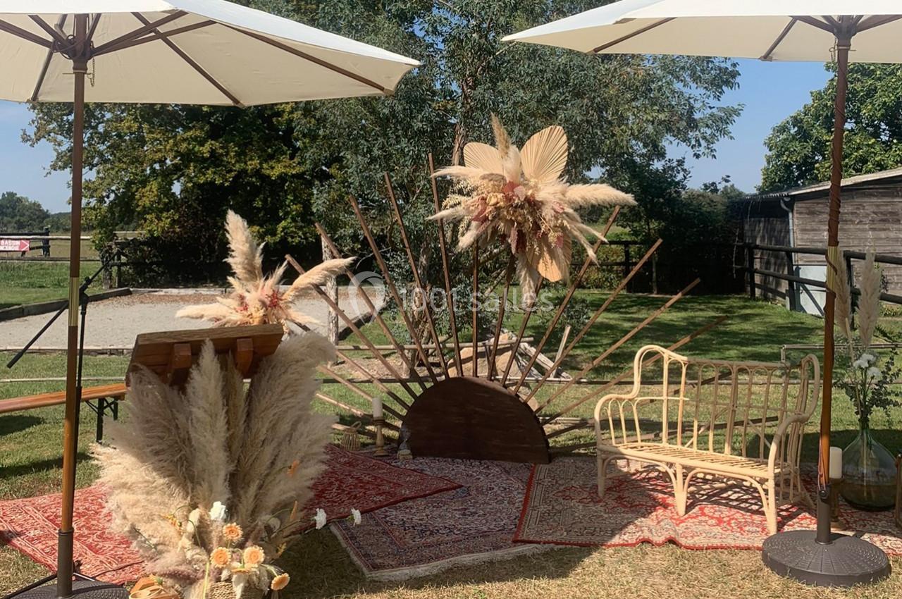 Décoration champêtre avec fleurs séchées, tapis, banc en rotin et parasols, installée en extérieur par temps ensoleillé.