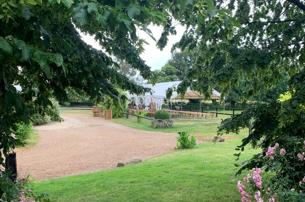 Vue d'un espace extérieur avec pelouse, allée gravillonnée et tente blanche entourée de végétation.