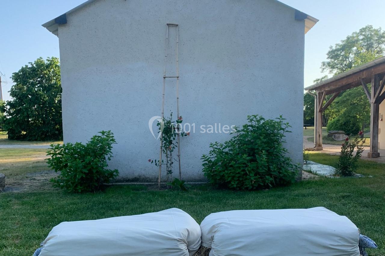 Deux coussins blancs posés sur des bottes de paille devant un mur blanc, entourés de verdure.