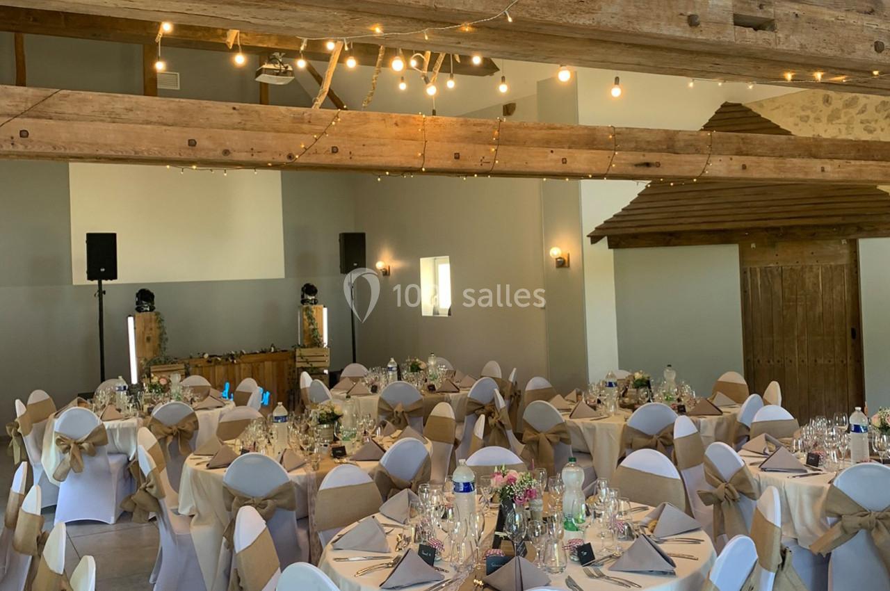 Salle de réception décorée avec des tables rondes dressées, des chaises ornées de nœuds et des guirlandes lumineuses…