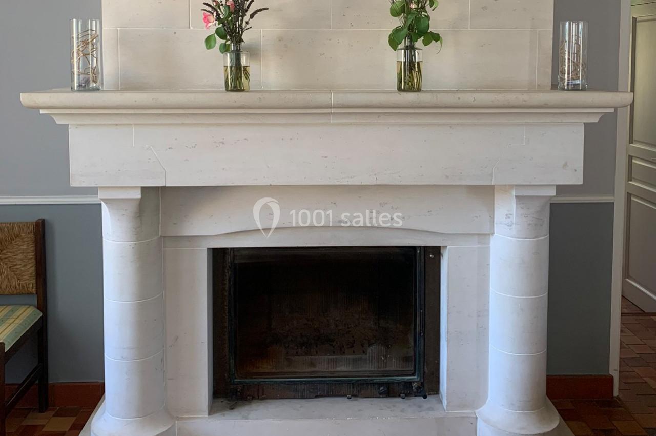Cheminée en pierre blanche avec deux vases de fleurs et deux bougies en verre posés sur le manteau.