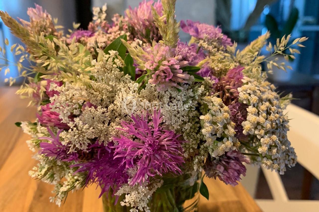 Bouquet de fleurs sauvages violettes et blanches dans un vase en verre, posé sur une table en bois.