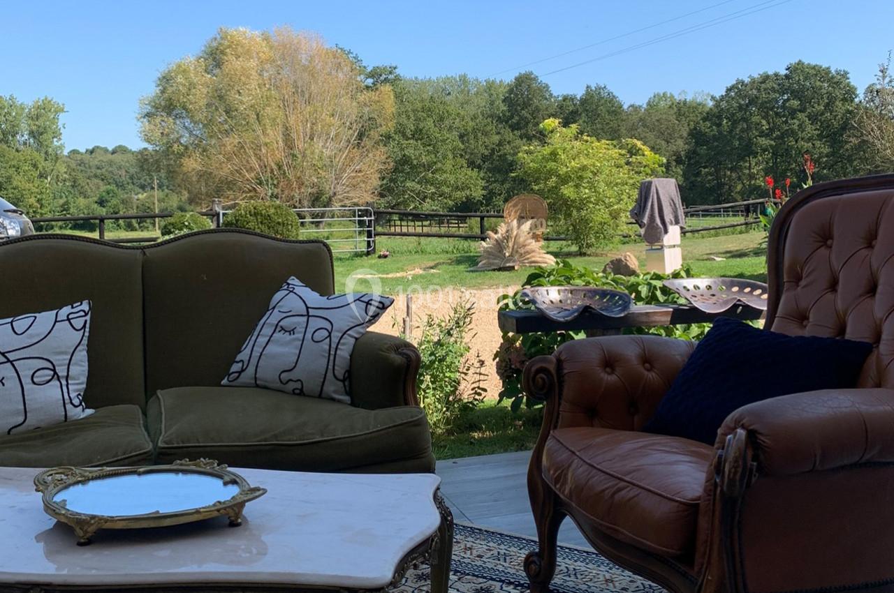 Deux fauteuils et une table basse sur une terrasse avec vue sur un jardin verdoyant et une clôture en arrière-plan.