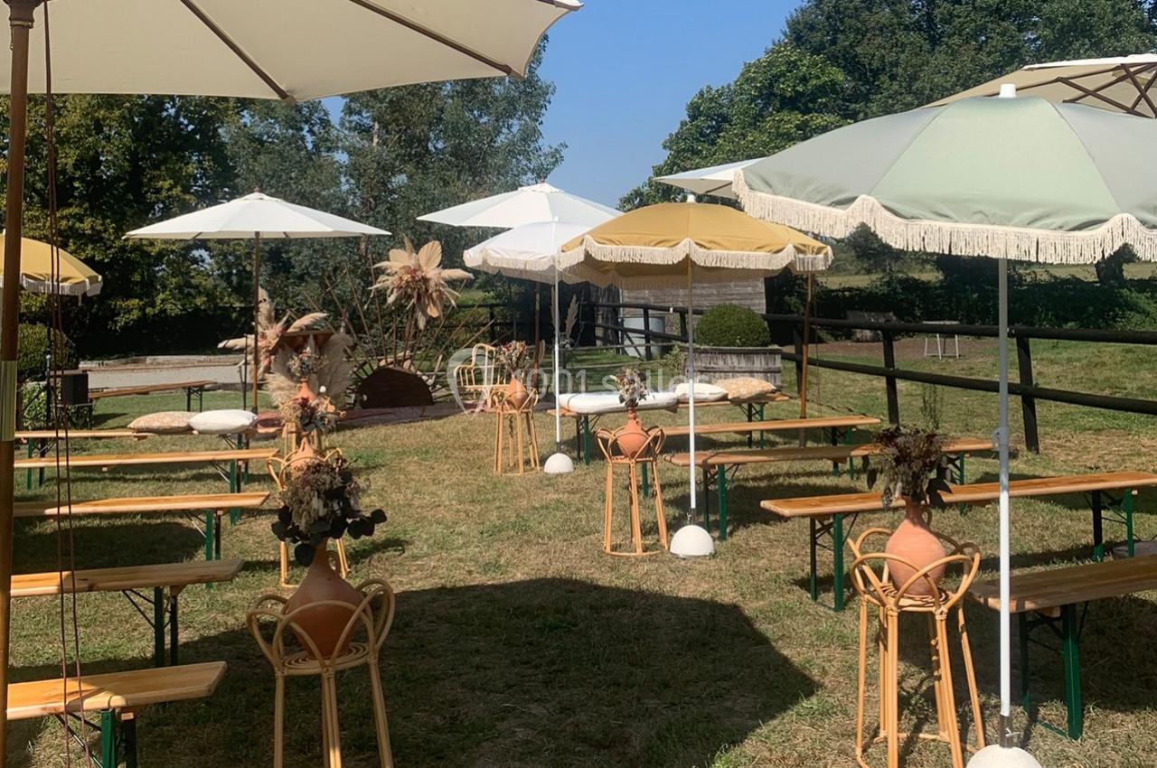 Terrasse extérieure avec tables en bois, parasols colorés et décorations florales, entourée de verdure.