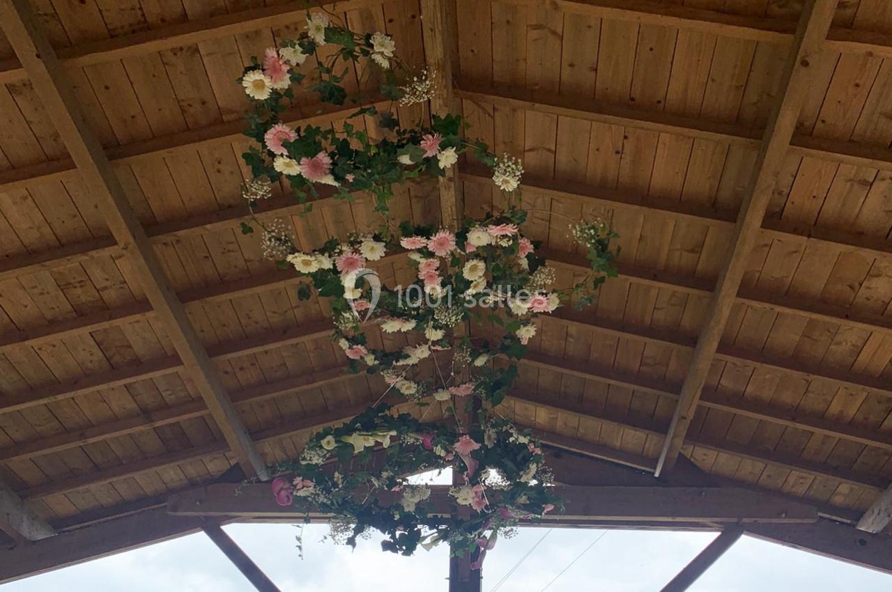 Guirlande florale suspendue sous une charpente en bois, composée de fleurs roses, blanches et de feuillage vert.