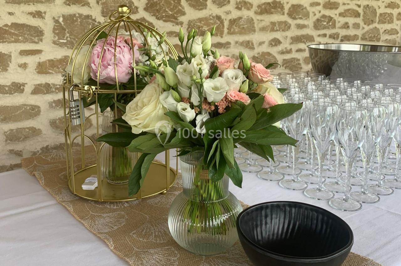 Bouquet de fleurs blanches et roses sur une table décorée, avec une cage dorée et des verres en arrière-plan.