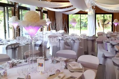 Structure en bois avec bancs alignés pour un événement, décorée de fleurs, avec un manoir en arrière-plan.