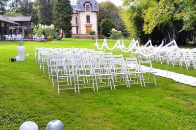 Structure en bois avec bancs alignés pour un événement, décorée de fleurs, avec un manoir en arrière-plan.