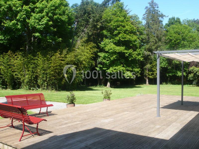 Terrasse en bois avec bancs rouges, pergola et vue sur un grand jardin arboré sous un ciel dégagé.