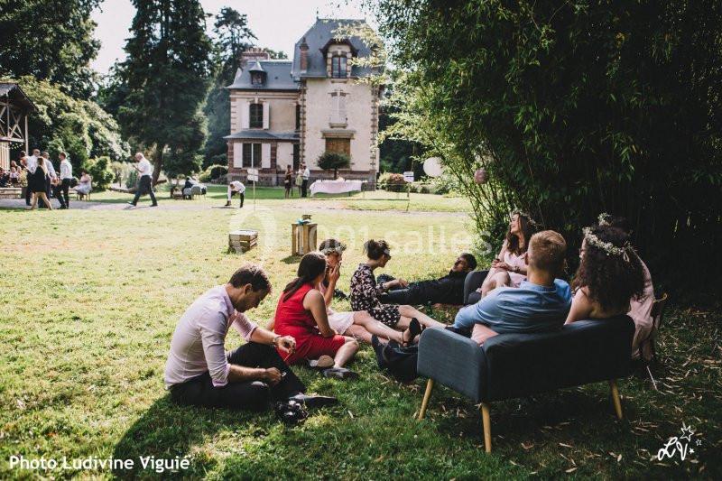 Groupe de personnes assises sur des fauteuils et l'herbe dans un jardin, devant une maison ancienne.