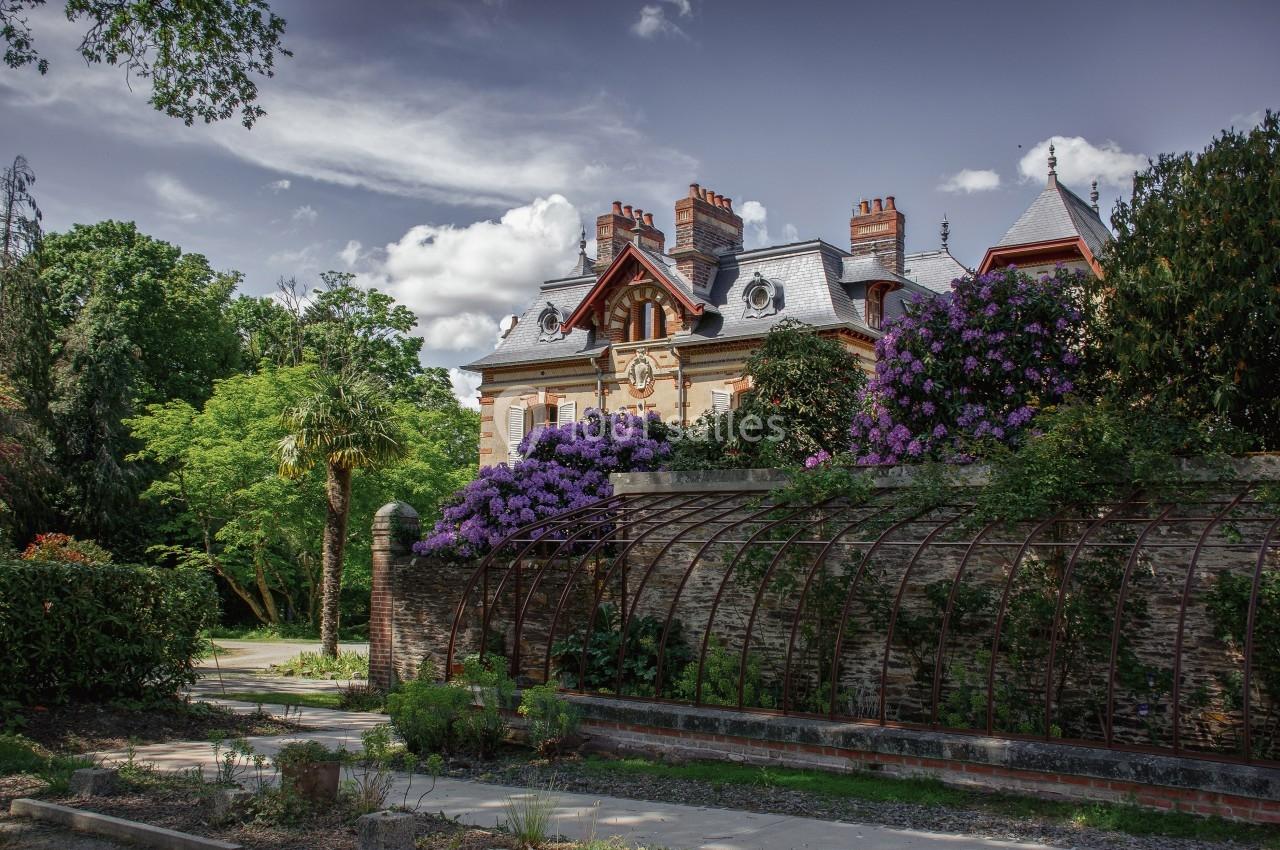 Manoir ancien entouré de jardins fleuris avec des rhododendrons violets et une structure métallique en premier plan.