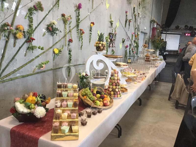 Table de buffet décorée avec des fruits, des pâtisseries, des macarons et des verrines, dans une salle ornée de fleurs…