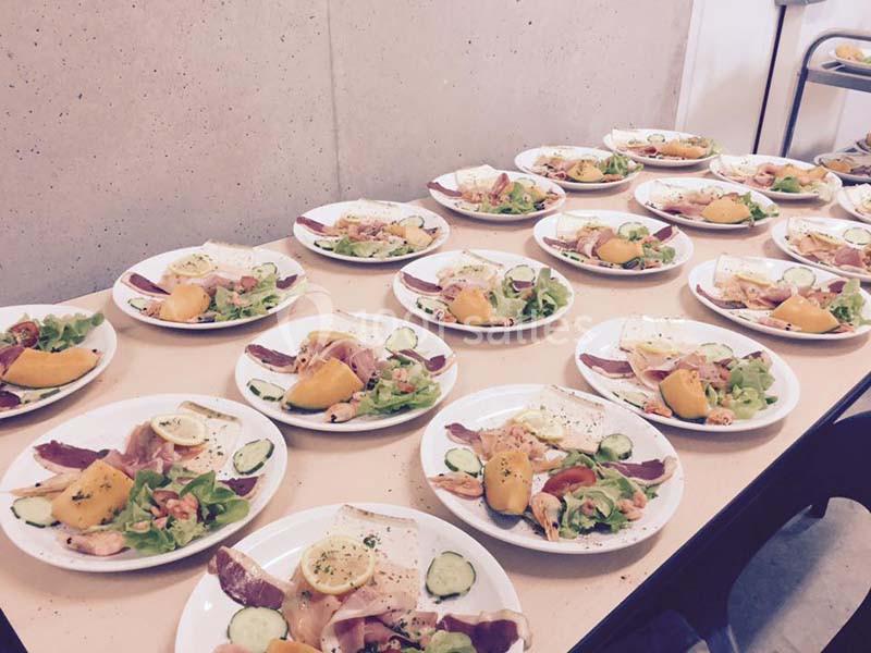 Assiettes dressées avec salade, charcuterie, fromage, légumes et fruits, alignées sur une table dans un cadre intérieur.