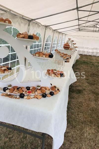 Buffet dressé sous une tente, avec des tables garnies de viennoiseries, desserts et verrines sur nappes blanches.
