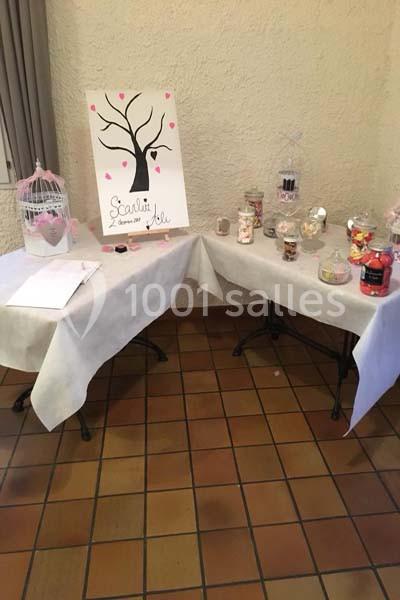 Deux tables décorées avec des bonbonnières, une cage blanche et un panneau illustré d'un arbre avec des cœurs roses.