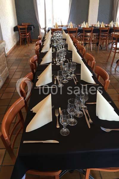 Table dressée avec nappes noires, serviettes pliées en triangle, verres et couverts alignés dans une salle carrelée.