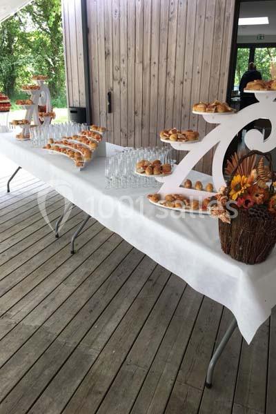 Table de buffet en extérieur avec pâtisseries, verres vides et décorations florales sur une nappe blanche.
