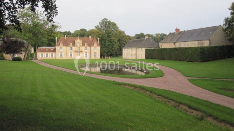 Manoir entouré de pelouses, d'un chemin en gravier et d'un petit étang, avec des arbres en arrière-plan.