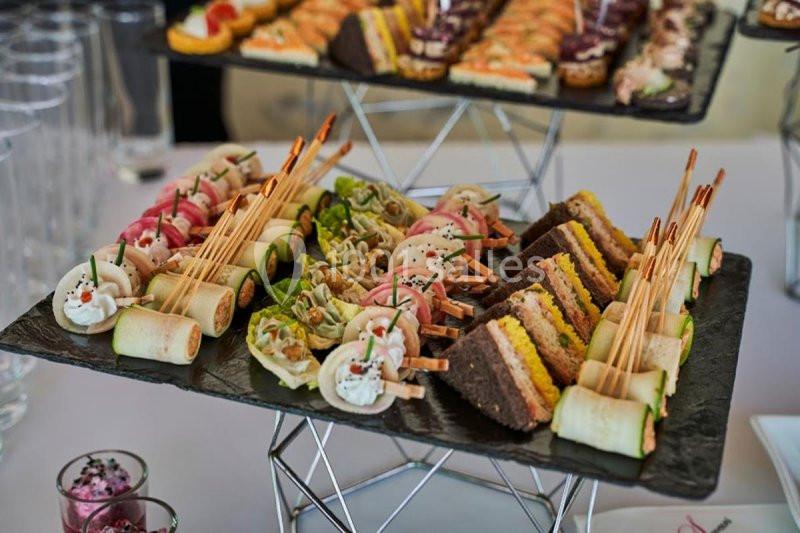 Plateaux de canapés variés avec des roulés, des mini-sandwichs et des amuse-bouches colorés sur une table de réception.