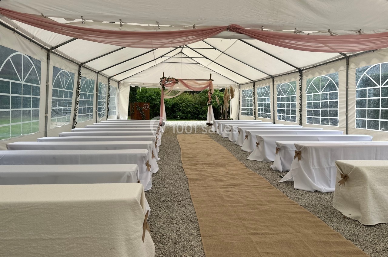 Intérieur d'une tente de réception avec allée centrale en toile, bancs et décoration pour une cérémonie en plein air.